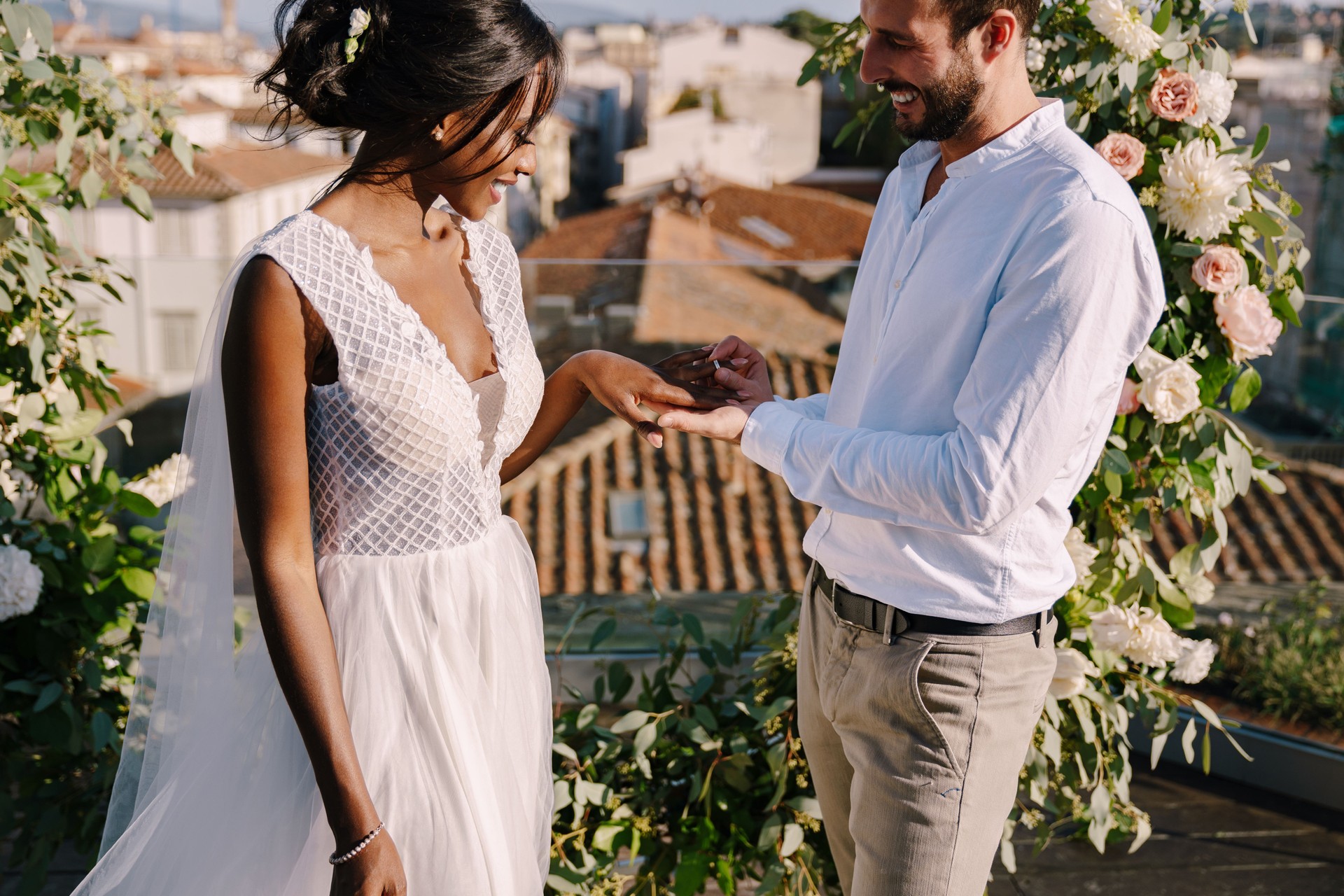 Mixed-race wedding couple - African-American bride and Caucasian groom. Groom puts a ring on brides finger. Destination fine-art wedding in Florence, Italy. Wedding ceremony on the roof